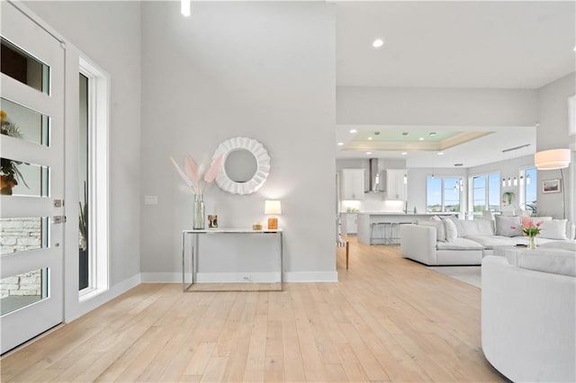 foyer entrance with light wood-style flooring, a tray ceiling, recessed lighting, and baseboards