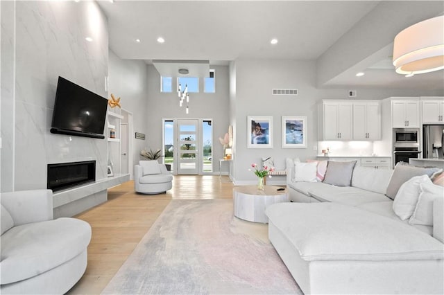 living area featuring light wood-type flooring, a high ceiling, recessed lighting, and a premium fireplace