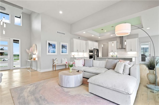 living room with light wood-style flooring, baseboards, recessed lighting, and a towering ceiling