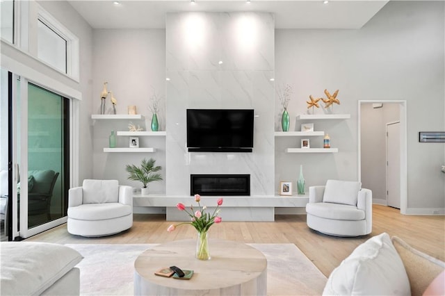 living area featuring light wood-type flooring, a high end fireplace, recessed lighting, baseboards, and a towering ceiling