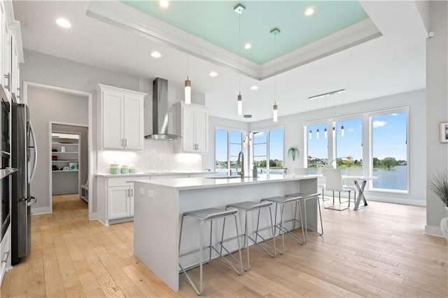 kitchen with wall chimney exhaust hood, a raised ceiling, a breakfast bar area, white cabinets, and recessed lighting
