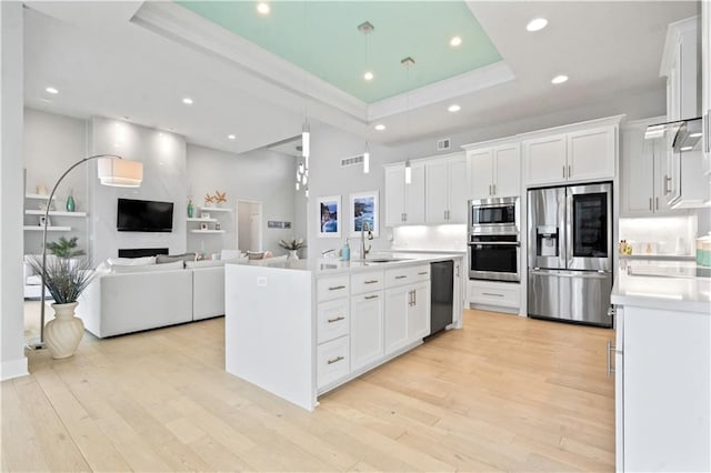 kitchen featuring stainless steel appliances, a tray ceiling, a sink, light countertops, and white cabinetry