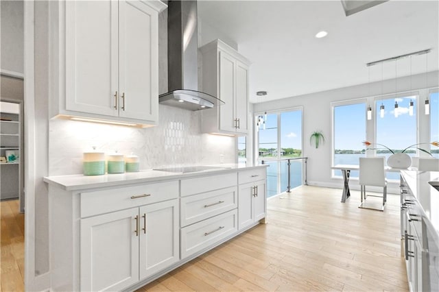 kitchen with wall chimney range hood, black electric cooktop, light wood-style floors, light countertops, and recessed lighting