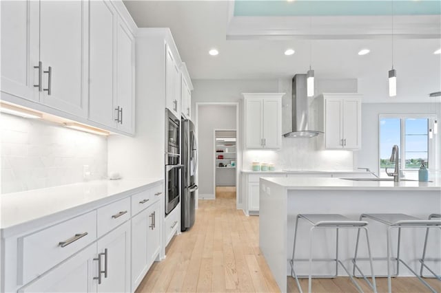 kitchen featuring wall chimney exhaust hood, appliances with stainless steel finishes, recessed lighting, a sink, and white cabinetry