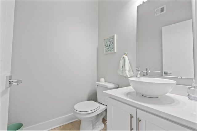 bathroom with toilet, vanity, wood finished floors, and baseboards