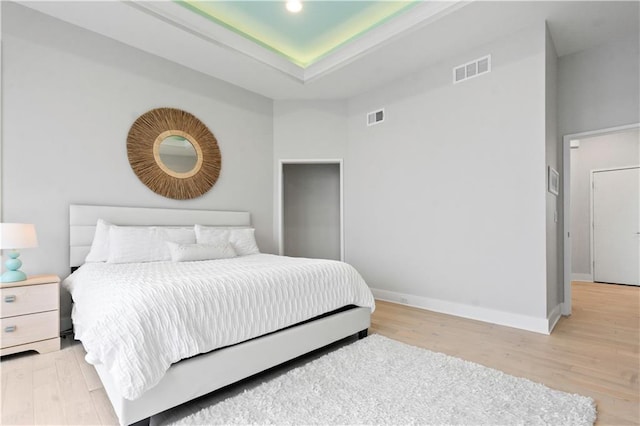 bedroom featuring light wood-style floors, a tray ceiling, and baseboards