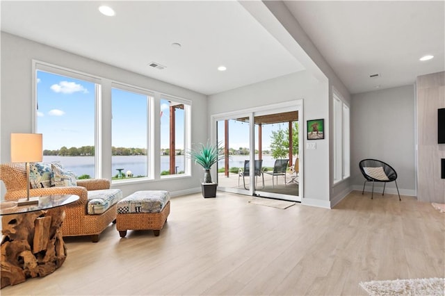 living area featuring light wood finished floors, a water view, recessed lighting, and baseboards