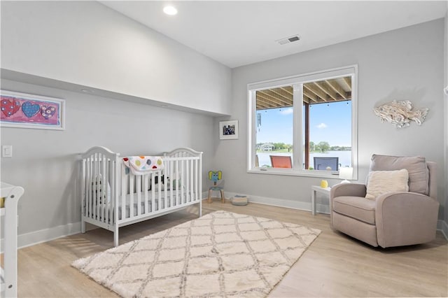 bedroom with wood finished floors, baseboards, and a nursery area