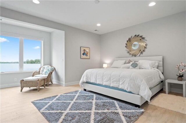 bedroom featuring light wood-style flooring, baseboards, recessed lighting, and a water view