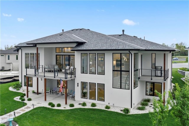 back of property with stucco siding, a patio area, a lawn, and a shingled roof