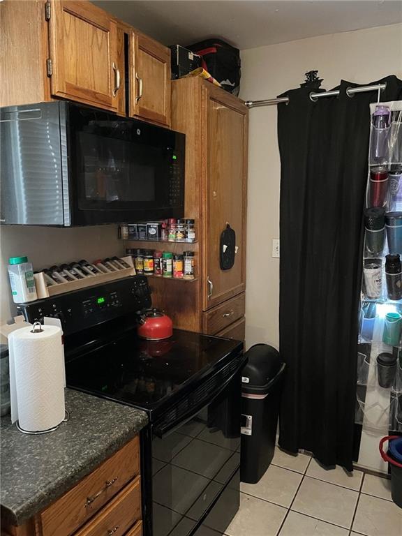 1114 Dakota St, Leavenworth, KS 66048 - kitchen with dark stone countertops, black appliances, light tile patterned floors, and brown cabinets