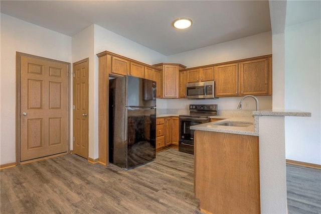 kitchen with a sink, brown cabinetry, black appliances, and wood finished floors
