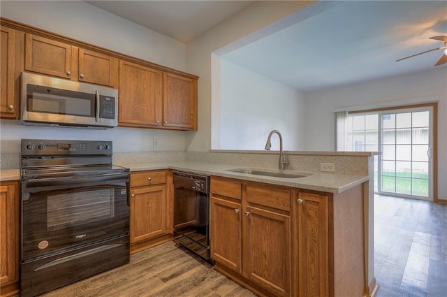 kitchen with light wood-style floors, a sink, brown cabinets, and black appliances