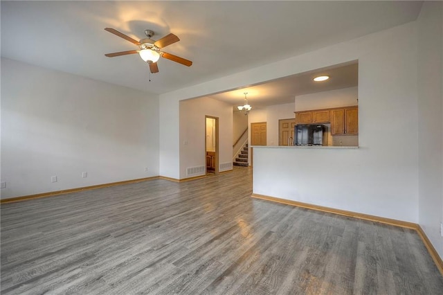 unfurnished living room with visible vents, wood finished floors, stairway, baseboards, and ceiling fan with notable chandelier