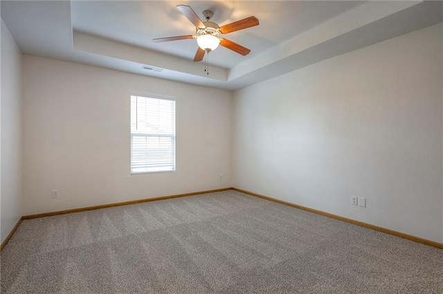 carpeted spare room featuring a tray ceiling, baseboards, and a ceiling fan