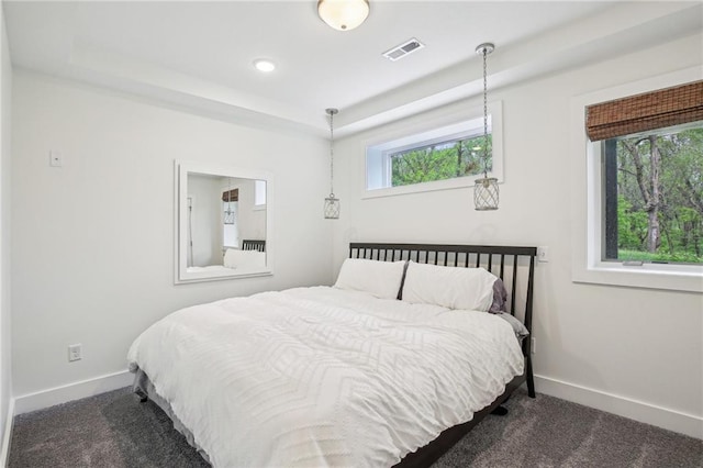 bedroom featuring a tray ceiling, visible vents, dark colored carpet, and baseboards