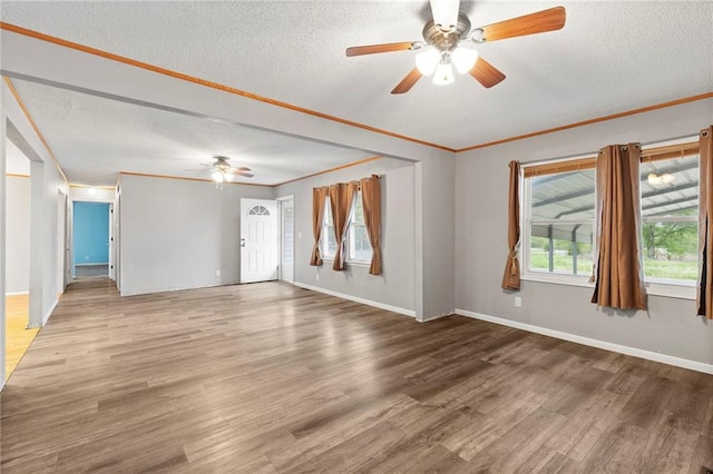 empty room with a textured ceiling, ceiling fan, wood finished floors, and crown molding