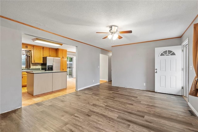 unfurnished living room with a ceiling fan, light wood finished floors, a textured ceiling, and crown molding