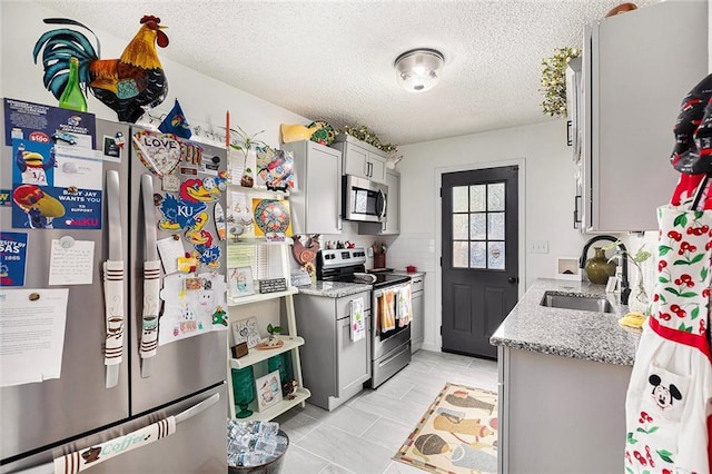kitchen featuring light stone countertops, appliances with stainless steel finishes, a sink, a textured ceiling, and light tile patterned flooring
