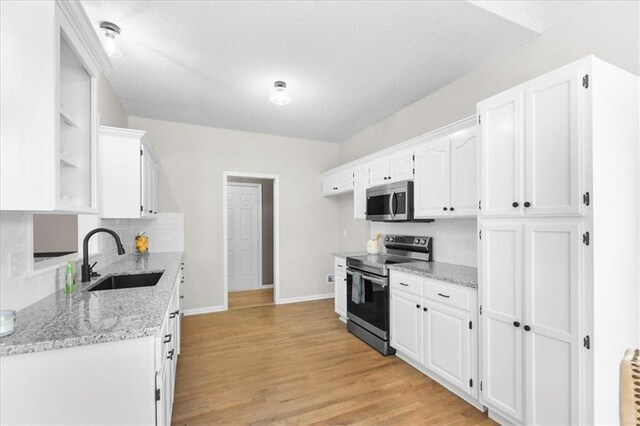 709 SW Graystone Dr, Grain Valley, MO 64029 - kitchen featuring appliances with stainless steel finishes, white cabinets, tasteful backsplash, light wood finished floors, and a textured ceiling