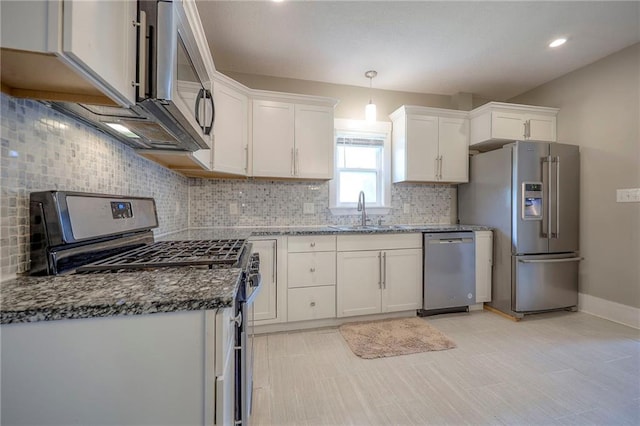 kitchen featuring appliances with stainless steel finishes, tasteful backsplash, a sink, dark stone countertops, and white cabinetry