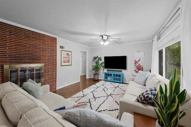 living room with crown molding, a brick fireplace, a ceiling fan, baseboards, and wood finished floors