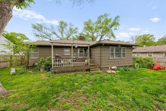 back of property featuring fence, a chimney, a lawn, and a deck
