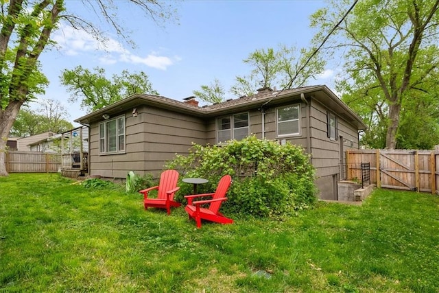 rear view of property featuring a fenced backyard, a gate, a chimney, and a yard