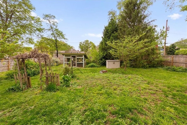 view of yard featuring a sunroom, fence, an outbuilding, and a storage unit