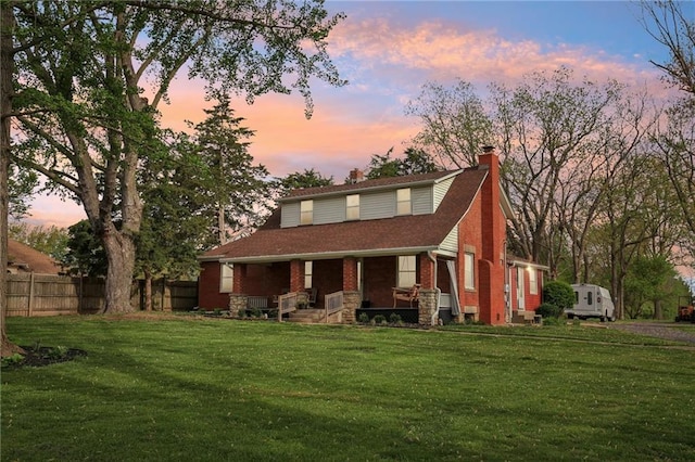 view of front facade featuring a chimney, a porch, a yard, brick siding, and fence