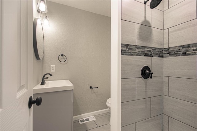 bathroom with visible vents, baseboards, toilet, vanity, and tiled shower