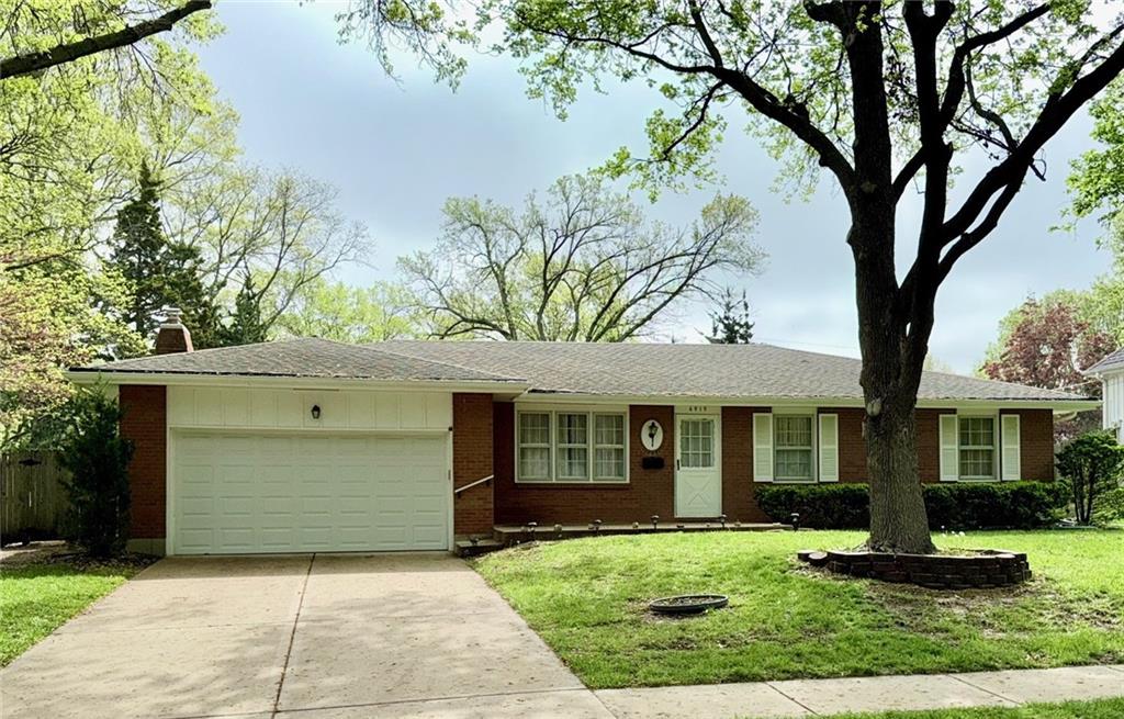 single story home with a front yard, a chimney, driveway, brick siding, and an attached garage