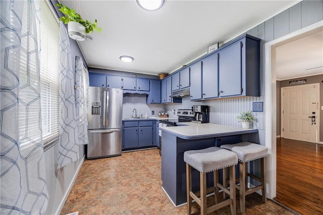 501 N Westwood Dr, Independence, MO 64050 - kitchen with appliances with stainless steel finishes, light countertops, a peninsula, under cabinet range hood, and blue cabinets