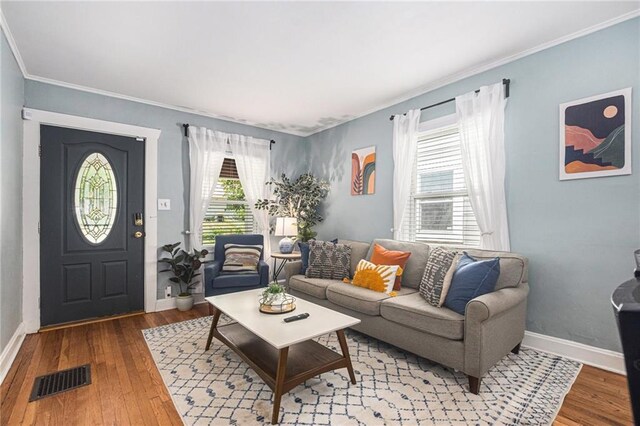 living area featuring visible vents, hardwood / wood-style flooring, ornamental molding, and baseboards
