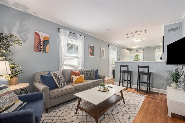 living room with ornamental molding, visible vents, baseboards, and light wood-style floors