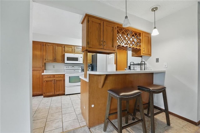 kitchen with white appliances, a peninsula, brown cabinets, decorative light fixtures, and light countertops
