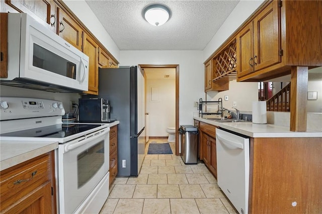 kitchen with white appliances, a sink, brown cabinets, a textured ceiling, and light countertops