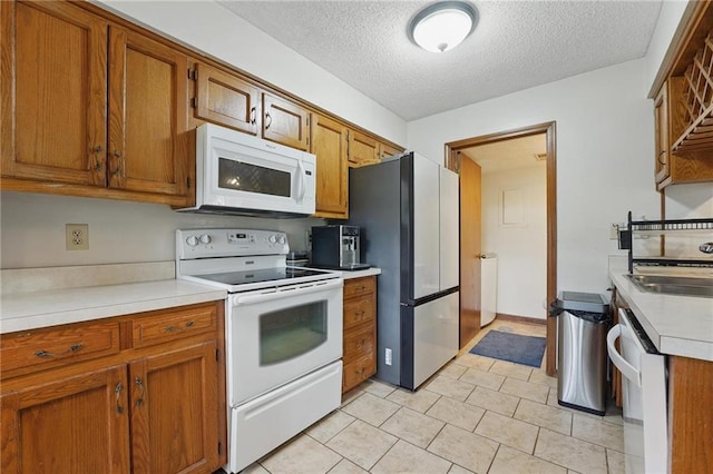kitchen featuring white appliances, brown cabinets, a textured ceiling, a sink, and light countertops