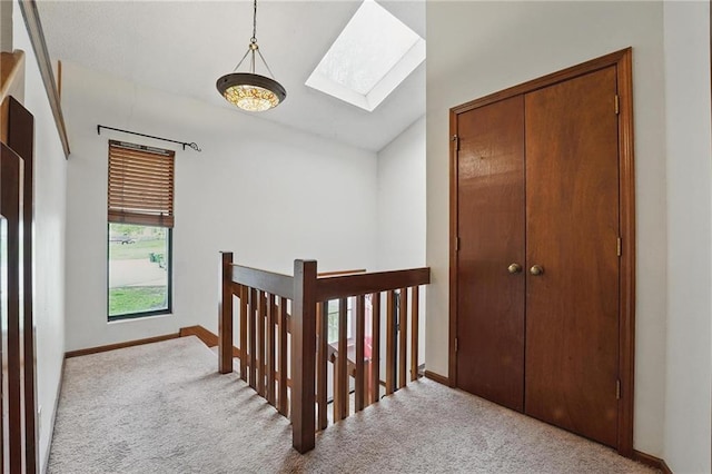 hallway featuring a skylight, lofted ceiling, carpet, baseboards, and an upstairs landing