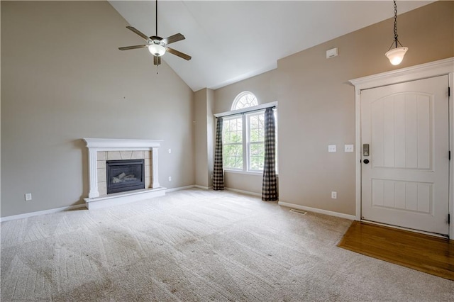 unfurnished living room featuring carpet flooring, high vaulted ceiling, a tiled fireplace, a ceiling fan, and baseboards