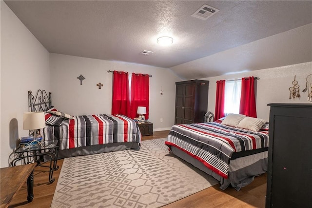 bedroom with a textured ceiling, visible vents, vaulted ceiling, and wood finished floors