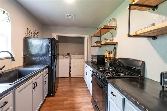 kitchen with a sink, independent washer and dryer, open shelves, black appliances, and dark countertops