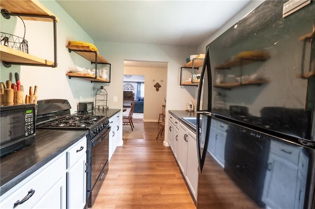 kitchen featuring open shelves, white cabinets, dark countertops, black appliances, and light wood finished floors