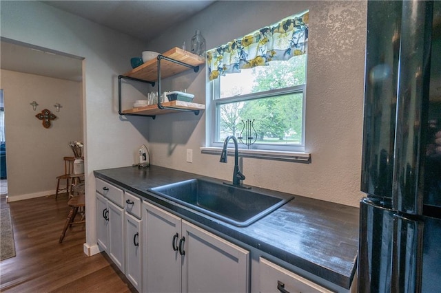 kitchen featuring freestanding refrigerator, dark countertops, a sink, white cabinetry, and dark wood-type flooring