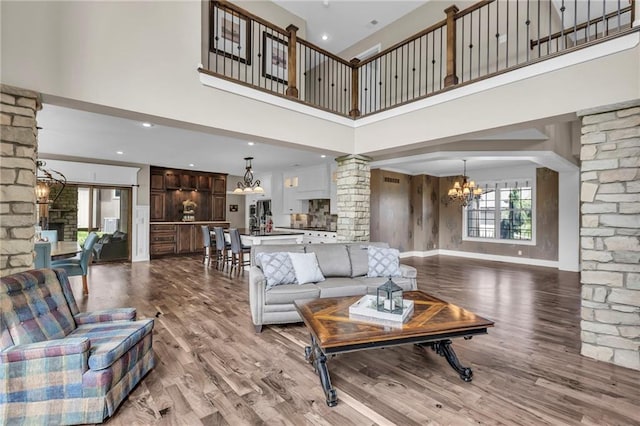 25203 W 97th Ter, Lenexa, KS 66227 - living room featuring decorative columns, a chandelier, a high ceiling, wood finished floors, and baseboards