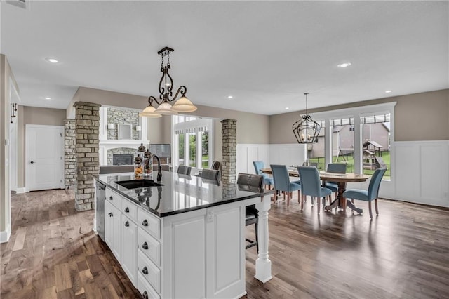 25203 W 97th Ter, Lenexa, KS 66227 - kitchen with a sink, dark countertops, a wainscoted wall, an island with sink, and a stone fireplace