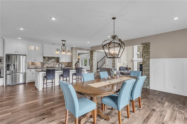 25203 W 97th Ter, Lenexa, KS 66227 - dining area featuring a chandelier, stairs, wood finished floors, a wainscoted wall, and a fireplace