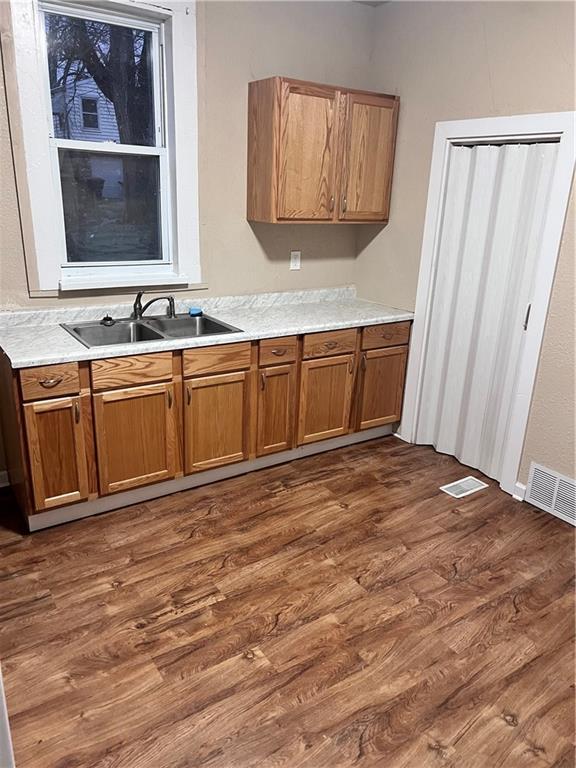kitchen featuring dark wood-style floors, a sink, brown cabinetry, and light countertops