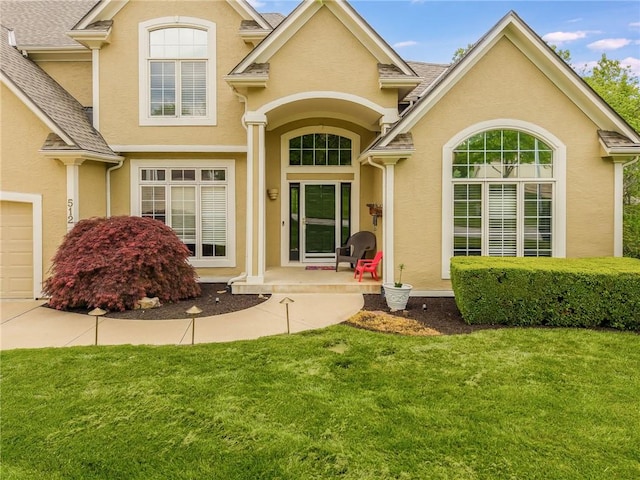 entrance to property with stucco siding, a lawn, and roof with shingles