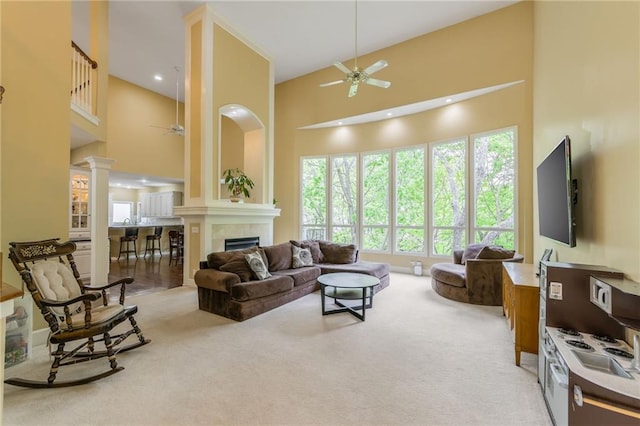 living area with a ceiling fan, a high ceiling, decorative columns, light carpet, and a tiled fireplace